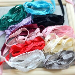 May include: A collection of ruffled elastic ribbon in various colors, including teal, black, red, white, and pink. The ribbons are bunched together, showcasing their texture and color variations. Ideal for crafting and sewing projects.