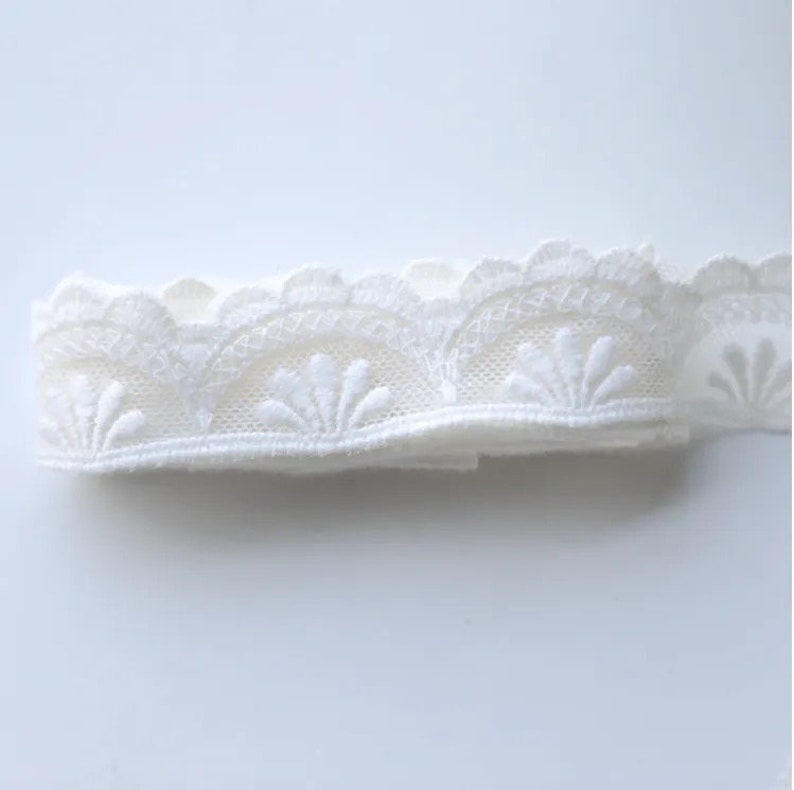 May include: White lace trim with a scalloped edge and a delicate floral pattern.