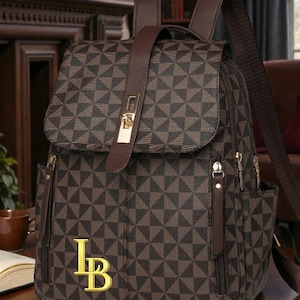 May include: A brown and black geometric patterned backpack. It features a flap closure with a gold buckle, side pockets, and adjustable straps. The text "LB" and "LuxeBagsByMSE" are displayed on the front of the bag.