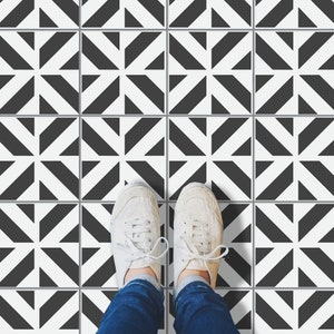 May include: Overhead shot of a person's feet wearing white canvas sneakers on a black and white patterned tile floor. The tiles have a geometric design with black and white triangles arranged in a starburst pattern.