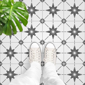 Puede incluir: Un par de zapatos de lona blancos con cordones negros se encuentran sobre un suelo de baldosas blanco y negro. Las baldosas presentan un patrón repetitivo de estrellas negras.