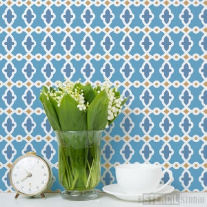 Puede incluir: Un papel tapiz con un patrón geométrico azul y dorado con un jarrón de flores blancas y una taza de té blanca y un platillo sobre una superficie blanca.