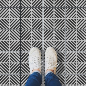 May include: A pair of white canvas sneakers with black laces stand on a black and white geometric patterned floor.