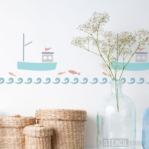 May include: A stencil design featuring a sailboat with a red flag, two fish, and a wavy line. The stencil is shown on a white wall with a vase of white flowers and wicker baskets in the foreground.