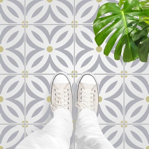 May include: A pair of white canvas shoes with black laces stand on a floor with a repeating pattern of gray and white floral shapes with yellow accents.