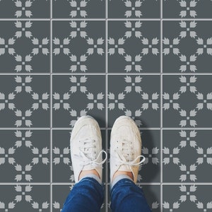 May include: A pair of white canvas sneakers with black laces are standing on a gray tiled floor with a white geometric pattern. The floor tiles are arranged in a grid pattern.