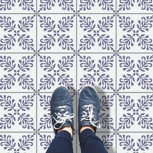 May include: A pair of blue sneakers with white laces stand on a white tiled floor with a repeating pattern of blue floral designs.