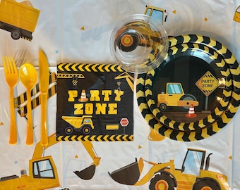May include: A construction-themed party set with yellow utensils, a plate, a napkin, and a clear cup. The plate and napkin feature construction vehicles and the words "Party Zone". The set is on a white tablecloth with construction vehicle designs.