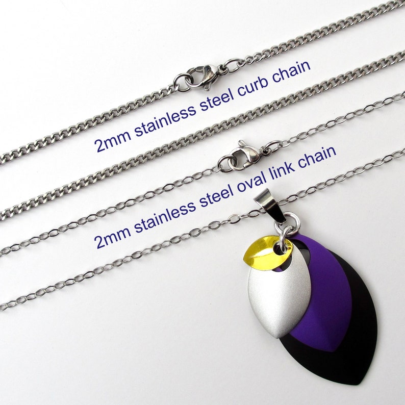 K&ouml;nnte beinhalten: Zwei Edelstahlketten, eine Gliederkette und eine ovale Gliederkette, beide 2 mm breit, mit einem Anh&auml;nger mit drei &uuml;bereinanderliegenden Bl&auml;ttern in Schwarz, Silber und Lila mit einem gelben Akzent.