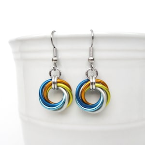 May include: A pair of silver hoop earrings with a knotted design. The knots are made of four strands of wire in blue, silver, yellow, and orange.