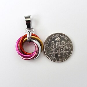 May include: A colorful pendant featuring interlocking rings in shades of pink, orange, gold, and silver. The pendant is shown next to a U.S. dime for size comparison. The pendant has a silver bail for attaching to a chain.