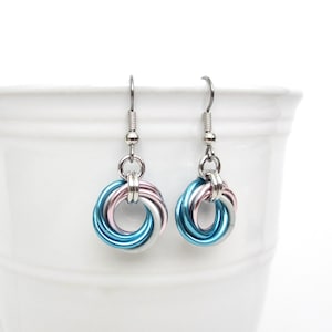May include: A pair of handmade earrings with a chainmail design. Each earring features a cluster of interlocking rings in blue, pink, and silver. The earrings hang from silver-colored ear wires, creating a modern and colorful accessory.