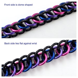 May include: A black, blue, and pink chainmail bracelet. The front side of the bracelet is dome shaped, while the back side lies flat against the wrist.