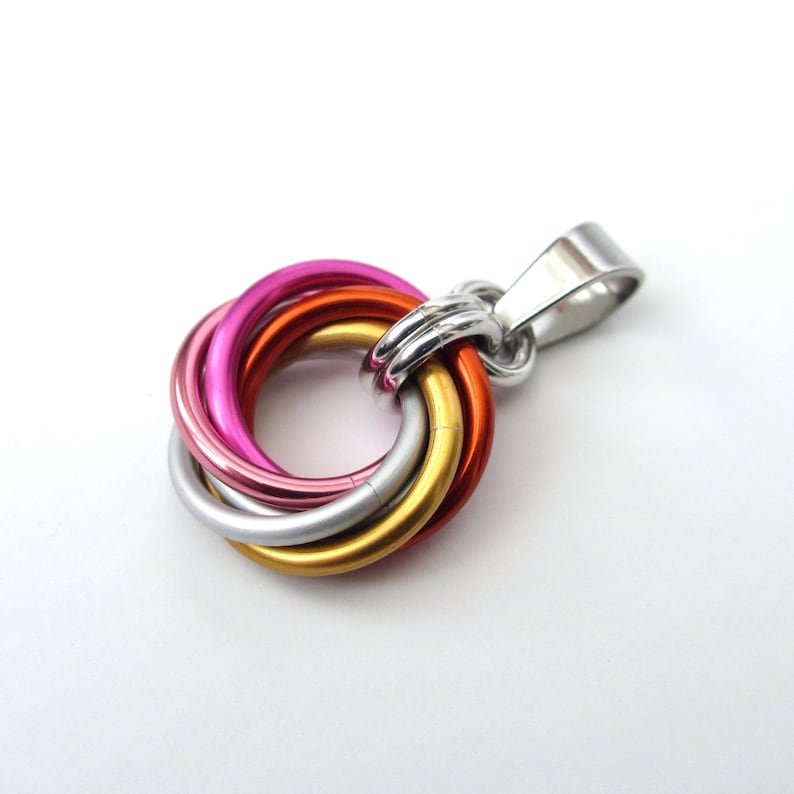 May include: A pendant featuring a cluster of colorful rings in pink, orange, gold, and silver, connected to a silver bail. The rings are intertwined, creating a unique, eye-catching design. The pendant is likely made of metal.