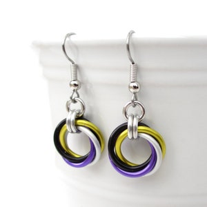 May include: A pair of silver dangle earrings with a ring of four colored wires. The wires are purple, black, white, and gold.