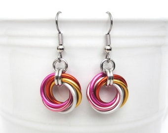 May include: A pair of silver dangle earrings with a knotted design. The knots are made of pink, orange, and silver colored wire.
