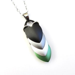 May include: A silver chain necklace with a pendant made of layered metal hearts in shades of green, white, and black.