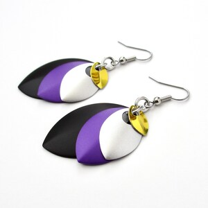 May include: A pair of earrings with three layered oval shapes in black, purple, and silver with gold accents. The earrings are attached to silver hooks.