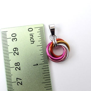 May include: A pendant with interlocking rings in silver, gold, orange, pink, and silver. The pendant is approximately 1 inch in diameter. The pendant has a silver bail for attaching to a chain.