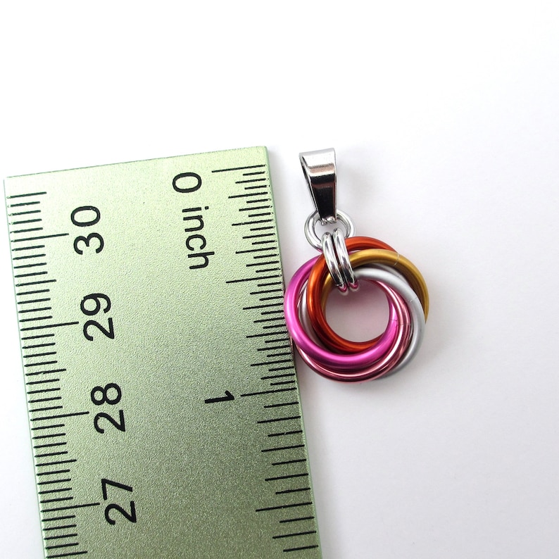May include: A pendant with interlocking rings in silver, gold, orange, pink, and silver. The pendant is approximately 1 inch in diameter. The pendant has a silver bail for attaching to a chain.