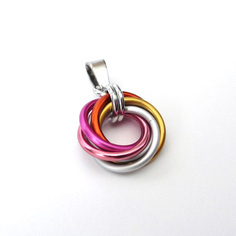May include: A pendant featuring a cluster of six interlocking rings in various colors: silver, gold, orange, pink, and purple. The pendant has a silver bail for attaching to a chain. The rings are made of metal.