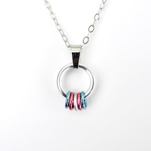 Peut inclure: Un collier argenté avec un grand pendentif circulaire. Le pendentif est orné de trois petits anneaux rouges, blancs et bleus. La chaîne est fine et le fermoir simple.