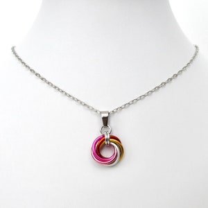 May include: A silver-toned necklace with a pendant featuring a colorful interlocking ring design. The pendant incorporates shades of pink, gold, and silver, suspended from a delicate chain. The necklace is displayed on a white mannequin.
