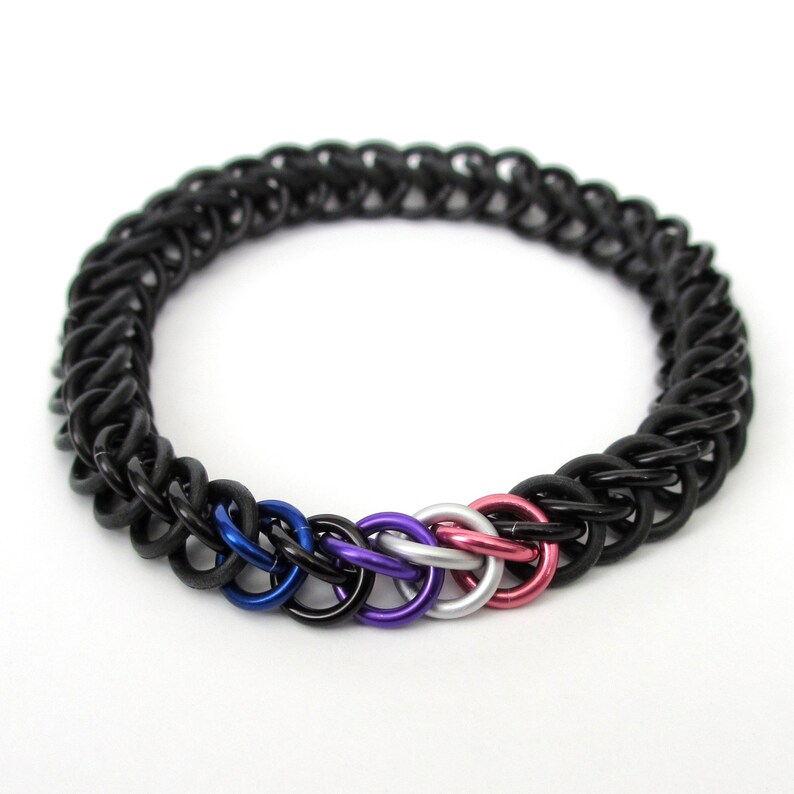 K&ouml;nnte beinhalten: Ein schwarzes Kettenhemdarmband mit einer Reihe von f&uuml;nf Ringen in den Farben der bisexuellen Pride-Flagge: Blau, Lila, Wei&szlig;, Grau und Rosa.