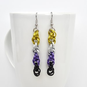 May include: A pair of handmade earrings with a chainmail design. The earrings feature a color gradient of gold, silver, purple, and black. The earrings are hanging in front of a white background.