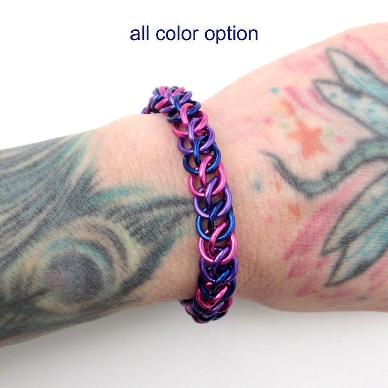 May include: A pink and blue chainmail bracelet. The bracelet is made of small metal rings that are linked together in a pattern. The bracelet is shown on a person's wrist.