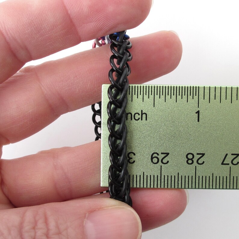 K&ouml;nnte beinhalten: Ein schwarzes Kettenhemdarmband, das mit einem Lineal gemessen wird. Das Armband ist etwa 2,5 cm lang.