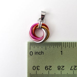 May include: A pendant with a silver bail and a circular design of interlocking rings. The rings are in shades of pink, orange, gold, and silver. The pendant is approximately 0.75 inches in diameter.
