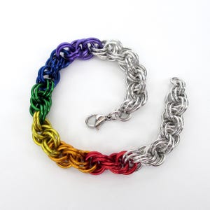 May include: A chainmail bracelet with a rainbow gradient of colours, transitioning from red to yellow, green, blue, and purple, and then to silver. The bracelet is made of interlocking metal rings and has a clasp closure.
