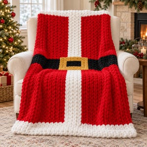 Könnte beinhalten: Eine grob gestrickte Wohndecke mit einem Weihnachtsmann-Anzug-Design. Die Decke ist überwiegend rot mit einem vertikalen weißen Streifen in der Mitte, einem horizontalen schwarzen Gürtel und einer quadratischen, goldfarbenen Schnalle.