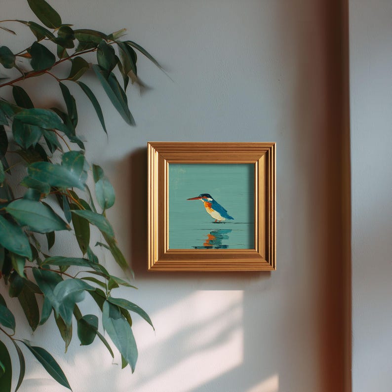 May include: A framed square painting of a kingfisher bird. The bird is depicted with blue, orange, and white feathers, standing in water. The painting is set against a teal background and framed in a gold-colored frame.