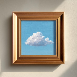 May include: A framed painting of a fluffy white cloud against a light blue sky. The artwork is encased in a gold-colored wooden frame, adding a touch of elegance to the simple yet striking landscape.
