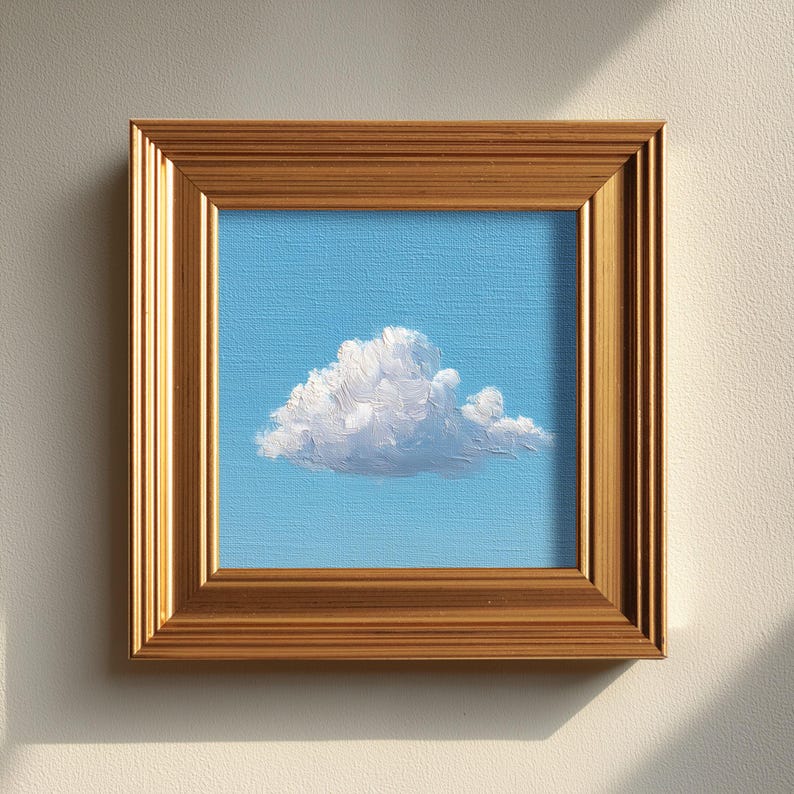 May include: A framed painting of a fluffy white cloud against a light blue sky. The artwork is encased in a gold-colored wooden frame, adding a touch of elegance to the simple yet striking landscape.