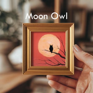 May include: A framed painting titled "Moon Owl" features a black owl perched on a tree branch against a red background with a large orange moon. The frame is gold-colored.