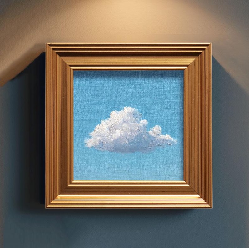 May include: A framed painting of a fluffy white cloud against a light blue sky. The artwork is encased in a gold-colored, rectangular frame. The painting evokes a sense of calm and serenity.