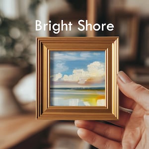 May include: A small framed painting with a gold-colored frame. The artwork depicts a seascape with a blue sky, white clouds, and a reflective body of water. The text "Bright Shore" is displayed at the top of the frame.