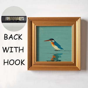 May include: Square framed art print featuring a colorful bird with a long beak standing in water. The bird has blue, white, and orange feathers. The frame is gold-colored. The back of the frame has a hook for hanging.