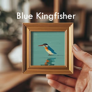 May include: A small framed painting of a blue kingfisher bird with a red beak, perched on a teal surface. The painting is in a gold-colored frame, and the text "Blue Kingfisher" is above the painting.