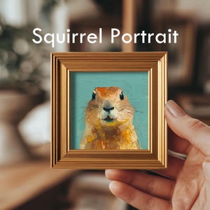 K&ouml;nnte beinhalten: Ein kleines, quadratisches Gem&auml;lde mit dem Titel "Squirrel Portrait" in einem goldenen Rahmen. Das Kunstwerk zeigt ein Eichh&ouml;rnchen mit orange-braunem Fell vor einem t&uuml;rkisfarbenen Hintergrund. Der Rahmen wird von einer Hand gehalten.