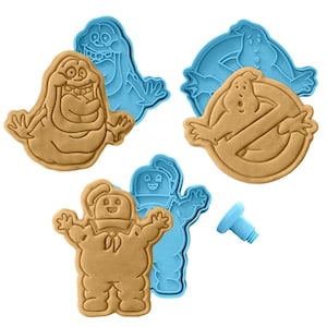 May include: A collection of cookie cutters featuring characters from Ghostbusters. The cutters are blue, and the cookies are tan. The set includes the Stay Puft Marshmallow Man, Slimer, and the Ghostbusters logo.