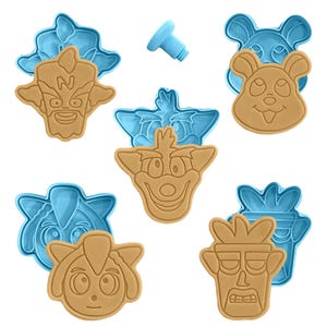 May include: A collection of tan-colored cookie cutters in various character face shapes, paired with light blue molds. A small, light blue plastic piece is also present. The cookie cutters are designed for baking and creating themed treats.