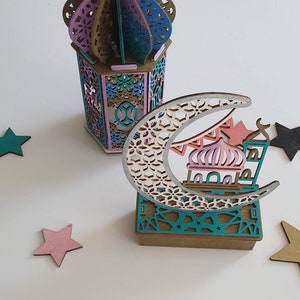May include: A wooden decorative set featuring a crescent moon with a mosque and stars, and a lantern with a colorful geometric design.