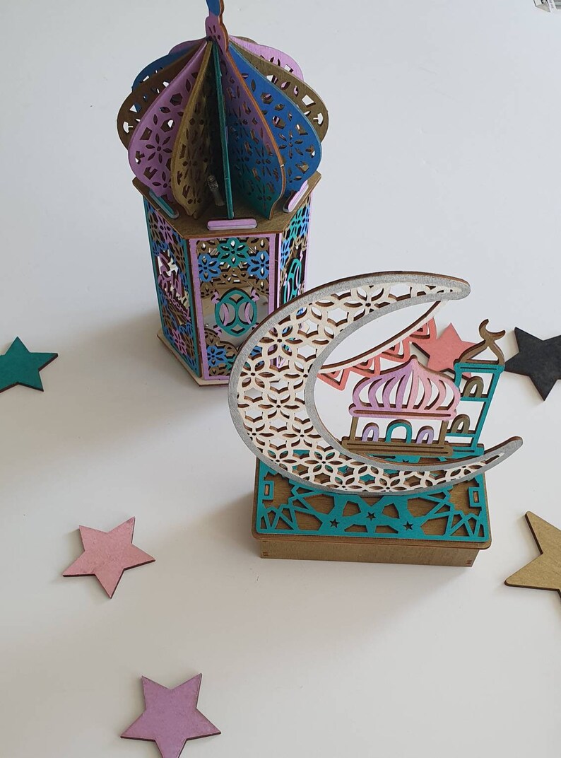 May include: A wooden decorative set featuring a crescent moon with a mosque and stars, and a lantern with a colorful geometric design.