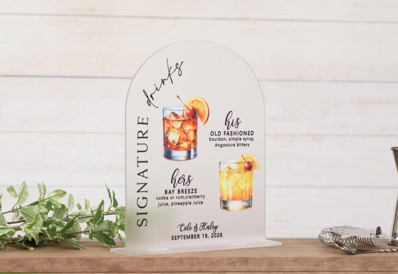 May include: An arched clear acrylic sign featuring the text SIGNATURE drinks, his OLD FASHIONED, and hers BAY BREEZE with illustrations of two cocktails, plus the names Cole & Haley and the date SEPTEMBER 19, 2026 printed in black ink.