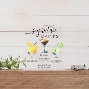 May include: An arched clear acrylic sign titled Signature Drinks featuring watercolor illustrations of a screwdriver, espresso martini, and margarita. Text includes The Fosters, David & Emily, March 14, 2026, and ingredient lists for each cocktail.