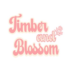 May include: A graphic design featuring the text Timber and Blossom in a soft pink, rounded, retro-style font. The word and has a wood grain texture, and a small, delicate pink floral illustration is positioned to the right of the text.